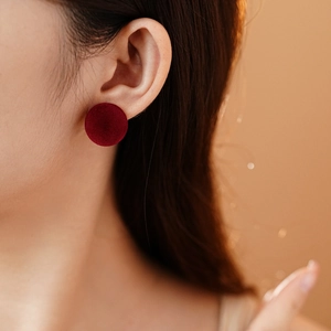 Detail view of a person wearing red velvet circular stud earrings with silver needles
