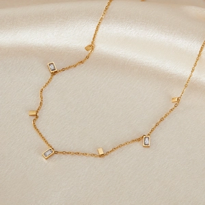 Macro detail of gold stainless steel necklace with rectangular zircons on silk background