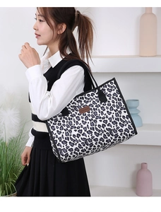 Detail of a large leopard print tote bag featuring black reinforced handles and brand tag