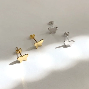 Macro shot of gold and silver butterfly stud earrings with soft shadows and elegant finish