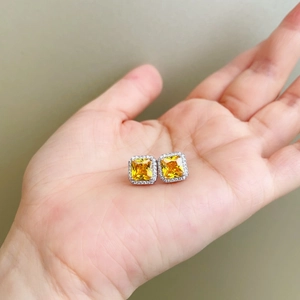 Close-up of square yellow gemstone earrings with white diamond halo on a palm