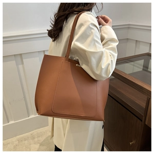 Side view of a large brown PU leather tote bag worn by a model in a minimalist setting