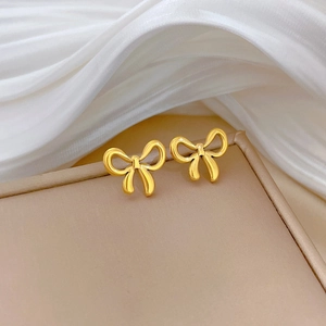 Detail shot of golden bow stud earrings on beige display box with white silk fabric