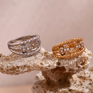 Close-up of twisted rope rings in gold and silver with clear gems on coral stone