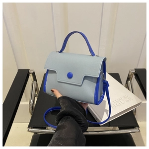 Detail of light blue textured leather handbag with contrast navy trim and button closure