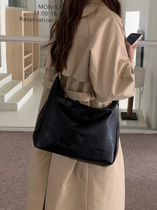 Close-up of a large black vintage shoulder bag in soft leather on a model in a trench coat