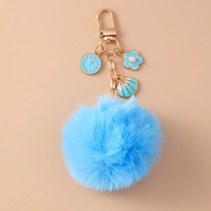 Close-up of blue faux rabbit fur keychain with gold clock flower and shell charms