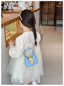 Detail of a blue and yellow PU leather handbag with a gold bow buckle on a girl