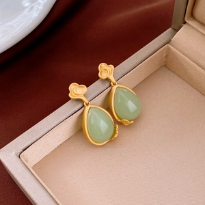 Macro detail of drop earrings featuring matte gold cloud motifs and green resin gemstones