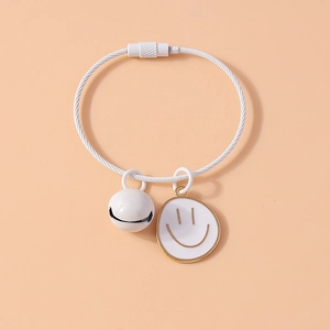 Detail of white braided bracelet featuring a bell, smiley face charm and metal swivel clasp
