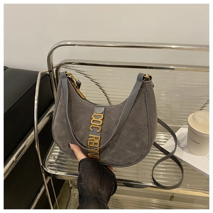Close-up of dark grey suede crescent bag with gold metal letters on a sleek shelf