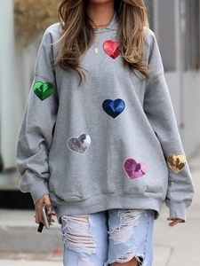 Close-up of colorful sequin heart patches on a grey oversized long-sleeved sweatshirt
