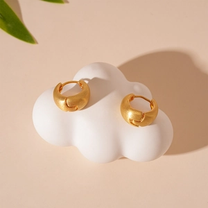 Close-up of golden brushed metal hoop earrings on a decorative white cloud prop