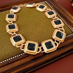 Vintage style gold necklace with square black enamel links displayed on green velvet