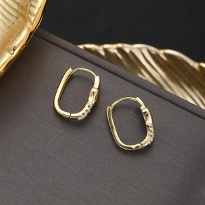 Macro view of gold geometric hoop earrings with sparkling cubic zirconia on a gray stand