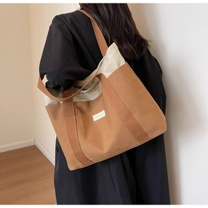 Brown and beige canvas tote bag shown on a shoulder with large capacity and logo label