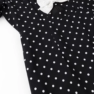 Detail of black polka dot dress with white bow accent and intricate fabric texture