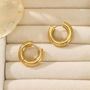 Detail of polished gold chunky hoop earrings displayed on a beige velvet jewelry box