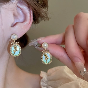 Detail of vintage gold rose relief earrings with light green base and pearl studs