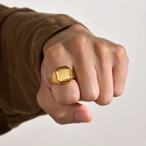 Close-up of a gold-finish octagonal signet ring worn on a hand with a clenched fist