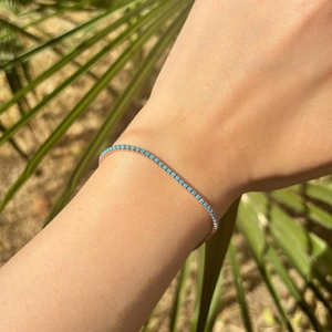 Close-up of a rose gold bracelet with circular teal stones on a wrist with palm background