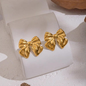 Elegant gold bow-shaped stainless steel earrings displayed on a white marble pedestal