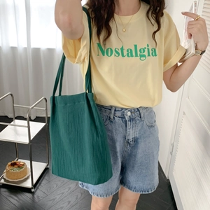 Close-up of a forest-green washed cotton linen tote bag styled with a casual summer outfit
