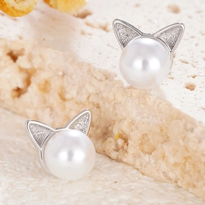 Detail of silver cat-ear stud earrings with large white pearls on a textured rock base