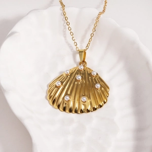 Vue détaillée du collier pendentif coquillage doré avec perles sur un plateau coquillage