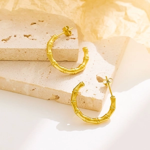Macro detail of French retro twisted gold hoop earrings on a warm travertine surface