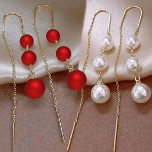 Detail of long gold tassel earrings with red frosted beads and white pearls for women