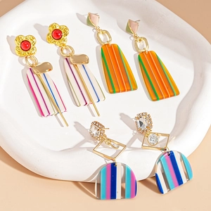 Three pairs of floral and geometric resin drop earrings on white ceramic tray