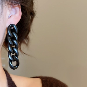 Close-up of matte black acrylic chain tassel earrings worn for a modern statement look