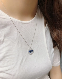 Detail of S925 sterling silver evil eye pendant necklace worn on a model with white t-shirt