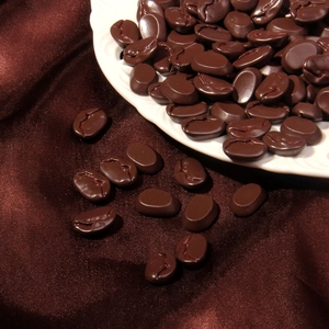 Realistische Kaffeebohnenmodelle aus Harz auf weißem Wellenteller über Seide