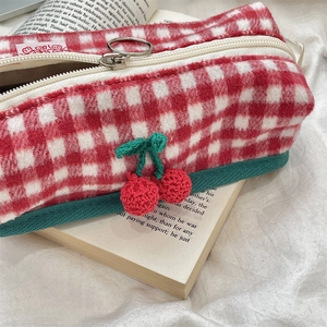 Close-up of red checkered knit pencil case with crochet cherry charm on an open book