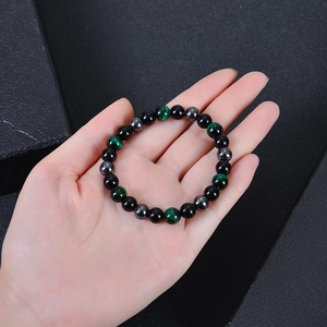 Main tenant un bracelet de perles de 8mm en oeil de tigre et pierre magnétique noire