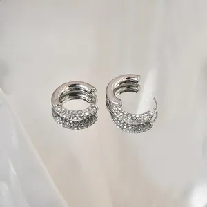 Macro shot of silver C-shaped hoop earrings with micro-paved zircons on white silk