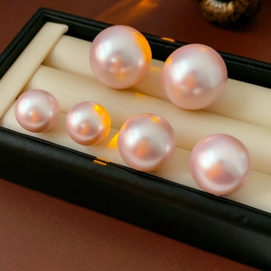 Detailed view of six round pink pearls with metallic luster in a black jewelry box
