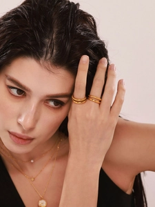 Detail of layered 18k gold-plated twisted rings and star pendant necklace on model