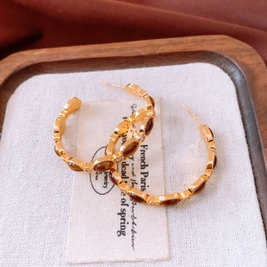 Détail macro de boucles d'oreilles C dorées avec pierres ambrées et accents de zircone