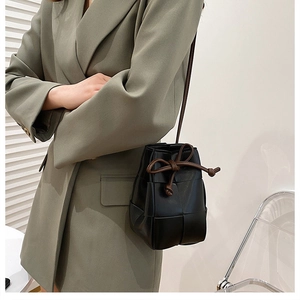 Detail of hand-woven black leather bucket bag with brown drawstring on a stylish model