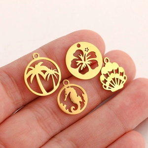 Detailed macro view of gold coconut tree, flower, seahorse, and shell charms on a finger