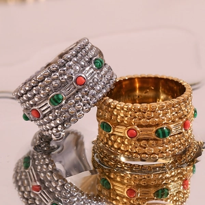 Close-up of gold and silver textured rings with red and green gemstone inlays