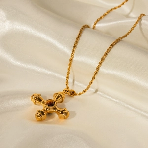 Close-up of 18k gold plated cross pendant with tiger eye stone on silk fabric