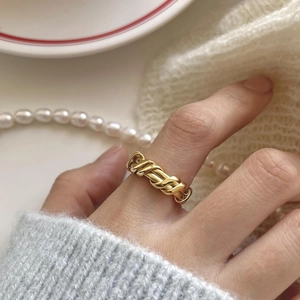 Detailed close-up of a gold woven texture ring worn on a finger in a lifestyle setting