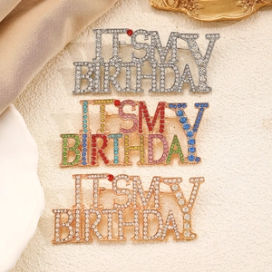Detailed view of three rhinestone brooches with It's My Birthday lettering in gold and silver