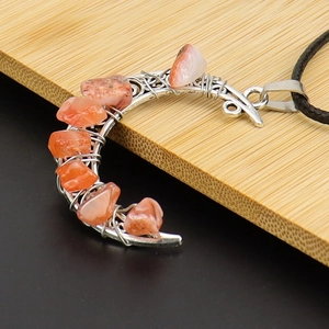 Close-up of crescent moon pendant with orange crystals on a bamboo surface