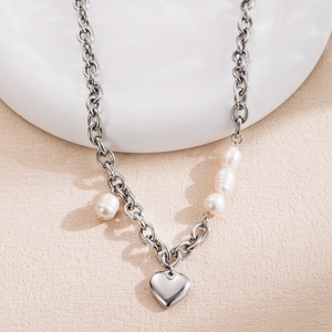 Collier à grosse maille argentée avec pendentif cœur et perles blanches sur fond beige