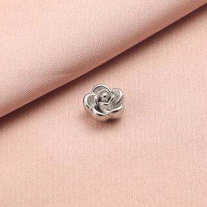 Close-up of a silver stainless steel rose flower bead on a soft pink textile background